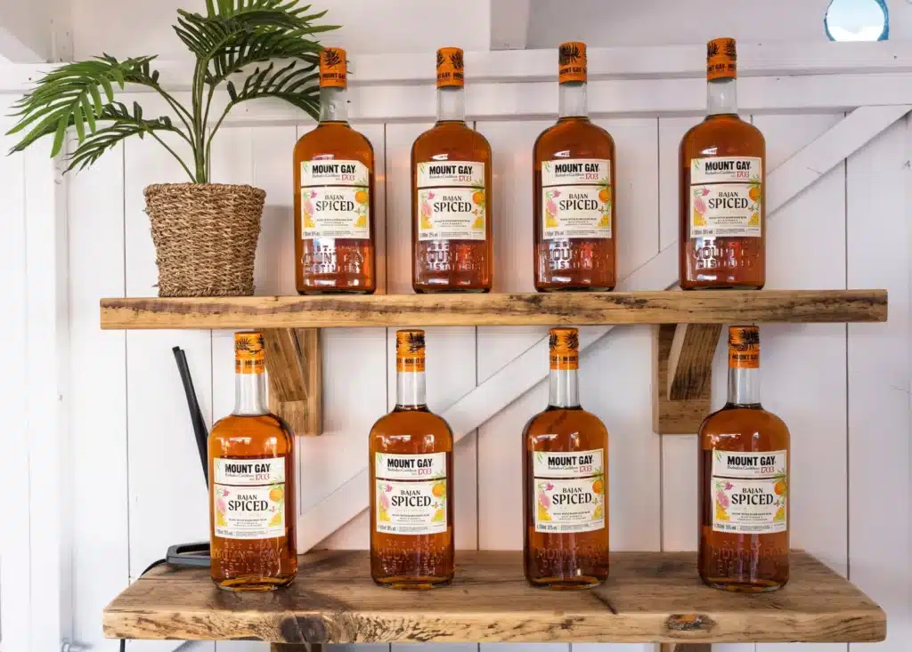 Eight bottles of Mount Gay Bajan Spiced on rustic wooden shelves at the Mount Gay Rum Shack.