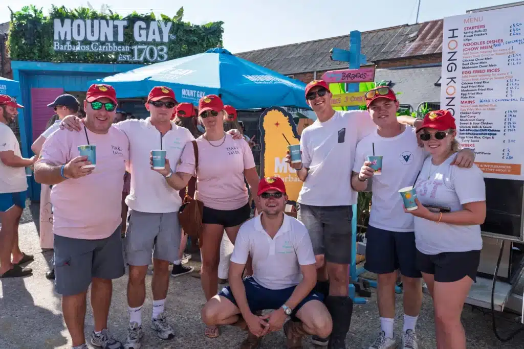 A sailing crew in matching shirts and Mount Gay Red Caps posing with cocktails outside the Rum Shack.