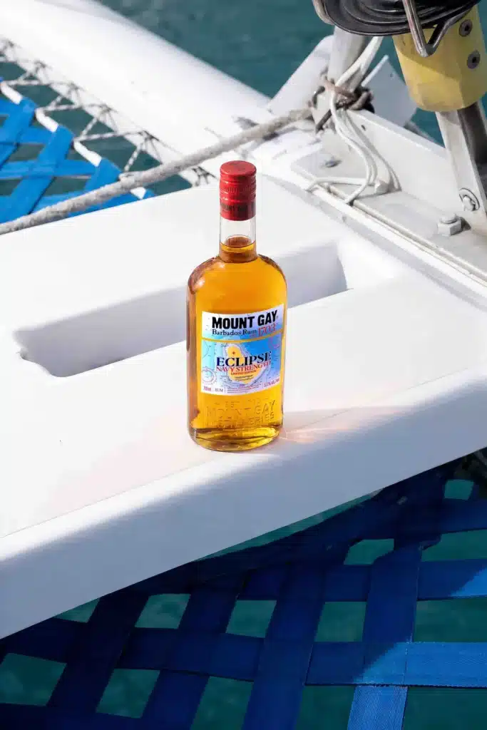 A bottle of Mount Gay Eclipse Navy Strength on the white hull of a catamaran above blue trampoline netting.