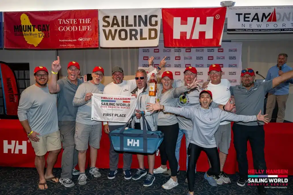 A first-place crew in Mount Gay Red Caps celebrating with a Helly Hansen Sailing World Regatta Series flag.