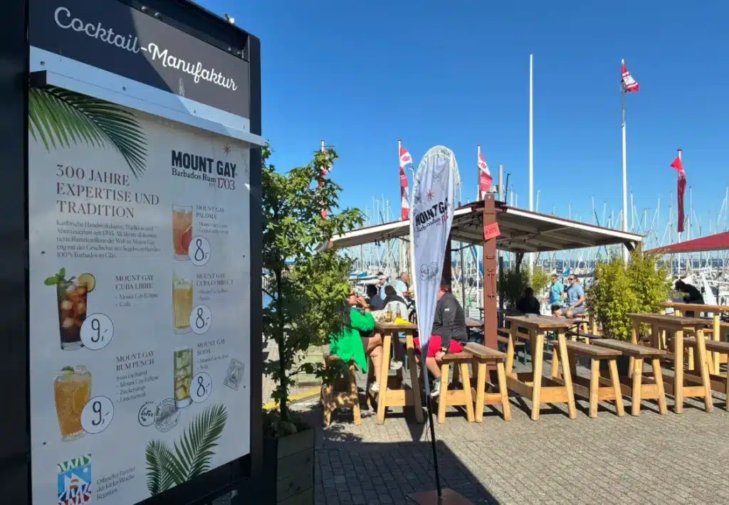 The Mount Gay cocktail menu board and outdoor bar seating beside the Schilksee marina at Kieler Woche.