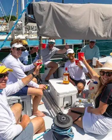 Sailors raising red cups on deck, with a bottle of Mount Gay rum on the cooler beside them.